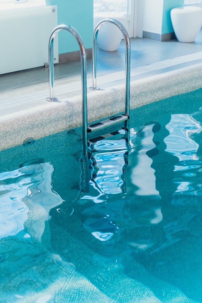 A serene view of an indoor swimming pool with a metal ladder and clear water.
