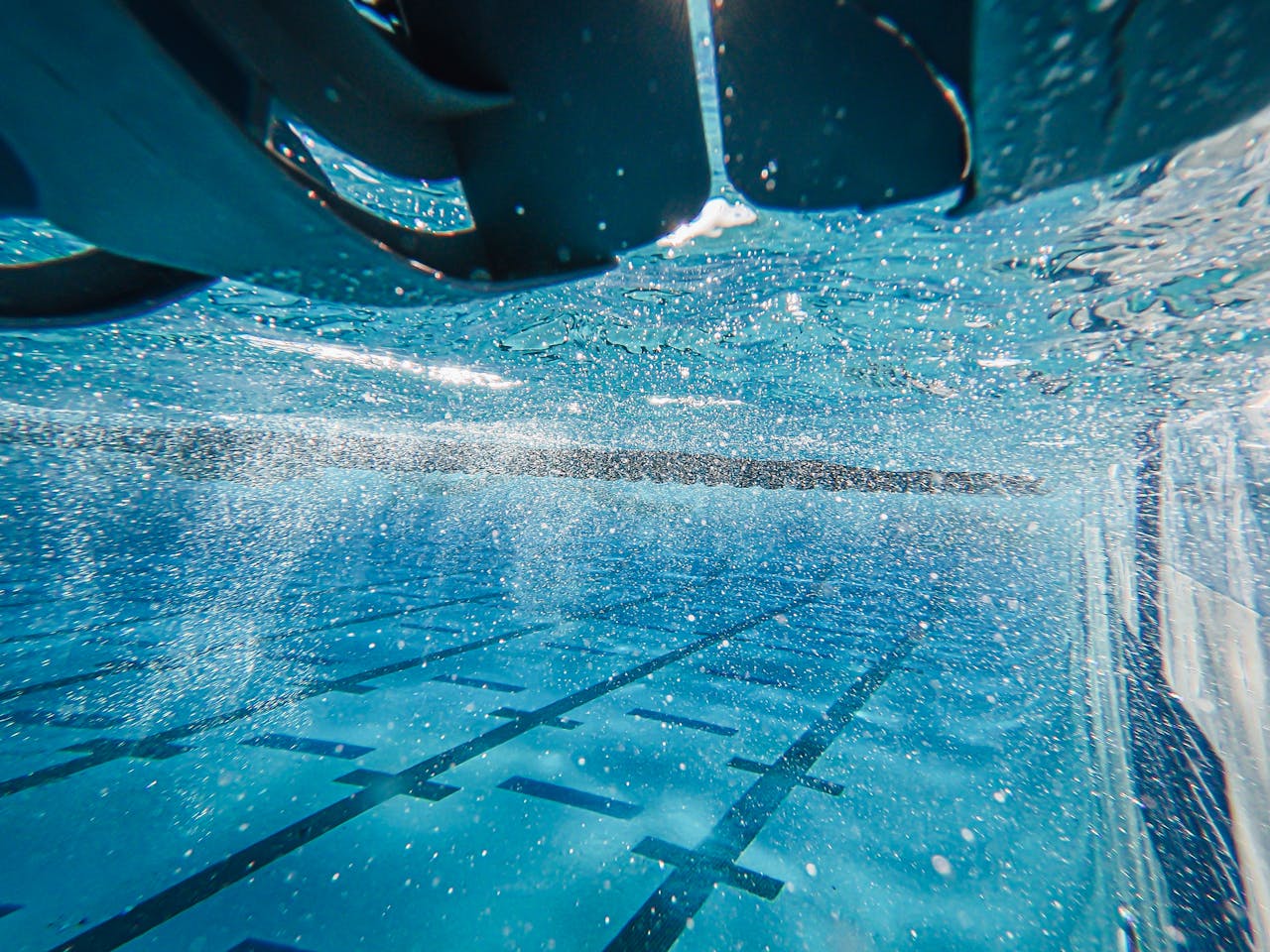 An underwater perspective capturing sparkling sunlight in a clear blue swimming pool.