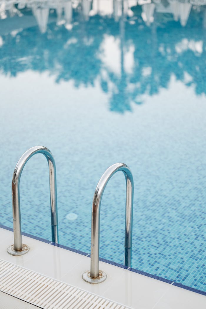 Clear swimming pool with stainless steel handrails and reflections of trees.